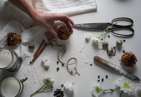 Vrouwelijke hand met cakes, melk en yoghurt in de cups, vanille, chrysant op een tafel. bovenaanzicht — Stockfoto