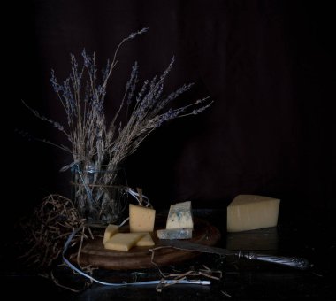 Natürmort. sert peynir, lavanta, antika gümüş bıçak ahşap masa üzerinde bir sürü. siyah arka plan