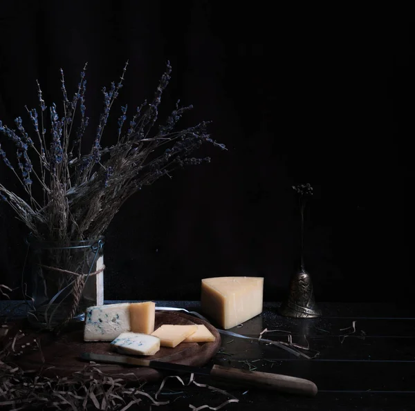 Naturaleza muerta. queso duro, racimo de lavanda, cuchillo antiguo en la mesa de madera. fondo negro — Foto de Stock