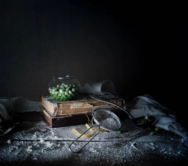 Vida morta rústica, vintage. ervilhas verdes, livros velhos, farinha em uma mesa de madeira. fundo escuro — Fotografia de Stock