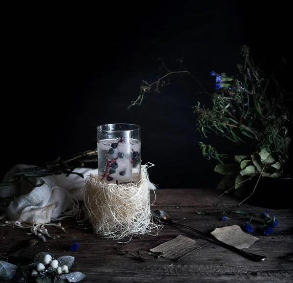 Stilleven, vintage. een glas mineraalwater en bessen, boeken, boeket op houten tafel. donkere achtergronden. . — Stockfoto