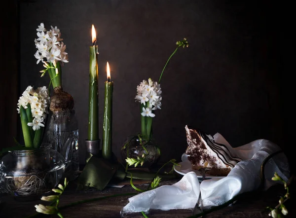 Drie witte hyacinth en fresia's in transparante vazen, kaars, taart op een donkere achtergrond — Stockfoto