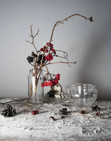 Натюрморт ветки вибурнума с ягодами и снегом в прозрачной вазе, стеклянный чайник на деревянном столе . — стоковое фото