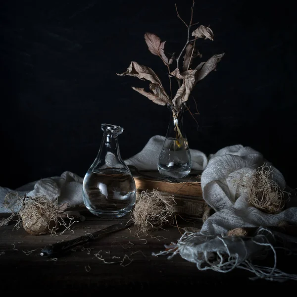 Natureza morta com cebolas e folhas secas em um vaso em uma mesa de madeira em um contexto escuro — Fotografia de Stock