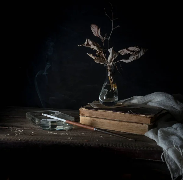 Stillleben mit alten Büchern, trockenen Blättern und dem Rauchen einer Zigarette. dunkler Hintergrund. Jahrgang — Stockfoto