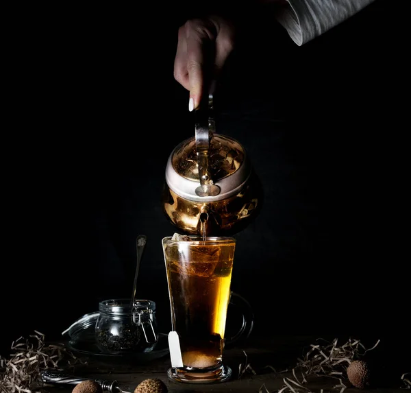 Vrouwelijke hand giet thee uit een gouden ketel. zwarte achtergrond — Stockfoto