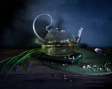 Kaynar su ve otların arasında bir cam çaydanlık. Koyu arka plan. Vintage.