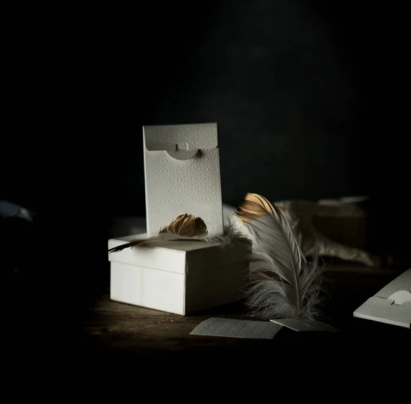 Stilleven. Witte vintage vakken, vergulde pluim op een houten tafel. Donkere achtergrond — Stockfoto