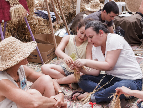 Woman showing girl how to weave a wreath of ears
