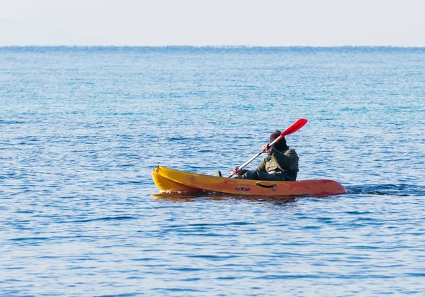 Fischer im grünen Overall schwimmt in orangefarbenem Kajak auf dem Meer — Stockfoto