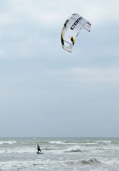 Jovem em terno impermeável escuro está envolvido em kiteboarding — Fotografia de Stock