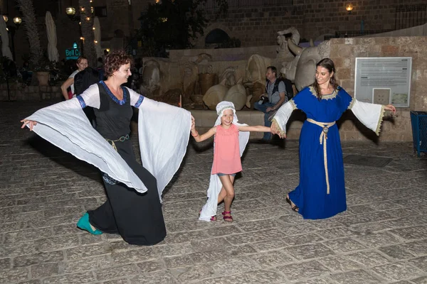 Две девушки - из клуба "Рыцари Иерусалима", одетые в традиционные костюмы средневековых дам, танцуют с девушкой ночью у фонтана в старом городе Яфо в Тель-Авиве-Яфо, Израиль — стоковое фото