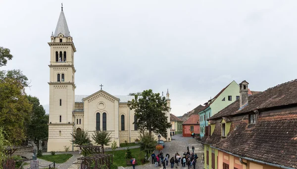 Les touristes se promènent autour de la place près de l'église catholique romaine - Citadelle dans le château de la vieille ville. Sighisoara ville en Roumanie — Photo