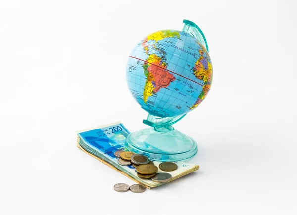 Egy persely, a globe formában történt, a Föld bolygó egy pénzt nyílás a tetején áll egy halom izraeli bankjegyek különböző érték és néhány érmét, elszigetelt fehér background. — Stock Fotó