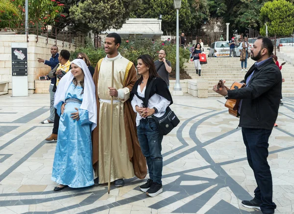 Una pareja casada marido y mujer embarazada en la ropa de la época de Jesús de pie con el ayudante y guitarrista en frente de la Basílica de la Anunciación en la antigua ciudad de Nazaret en Israel — Foto de Stock