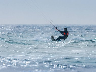 Karanlık su geçirmez elbiseli genç adam kiteboarding Akdeniz denize yakın Nahariyya, İsrail üzerinde rüzgarlı havalarda devreye girer