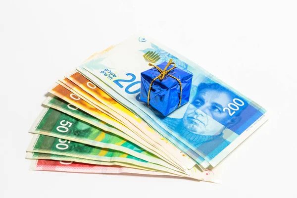 Moneta israeliana di nuove banconote israeliane di diverso valore in shekel (NIS) con una scatola blu decorativa che rappresenta un regalo, isolata su uno sfondo bianco — Foto Stock