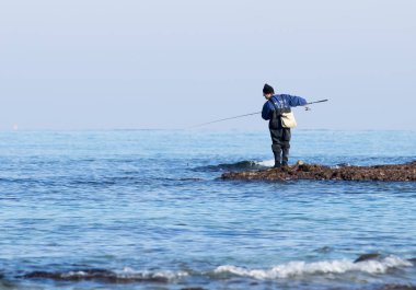 Balıkçı bir balık kış sabahı, bir iplik üzerinde Rosh Hanikra, İsrail yakınındaki plajda yakalar