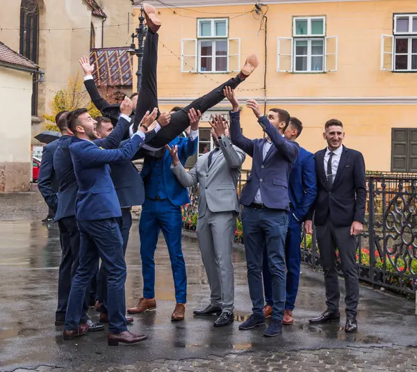 Vrienden van de bruidegom gooi hem in de lucht voor de kerk op het kleine plein. Sibiu stad in Roemenië — Stockfoto