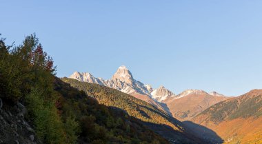 Dağların panoramik manzarası ve kar altında Ushguli zirvesi, Gürcistan 'ın dağlık kesiminde, gün batımında görülebilir.