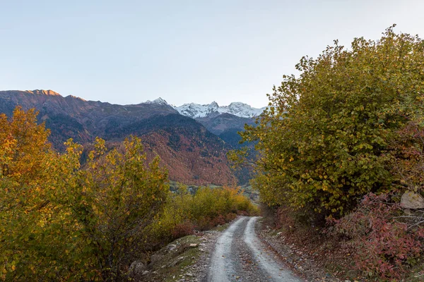 Panoramic view of a mountain road passing through mountains and peaks in the snow, visible in the distance, in the mountainous part of Georgia - Svaneti at sunset — Stock Photo, Image