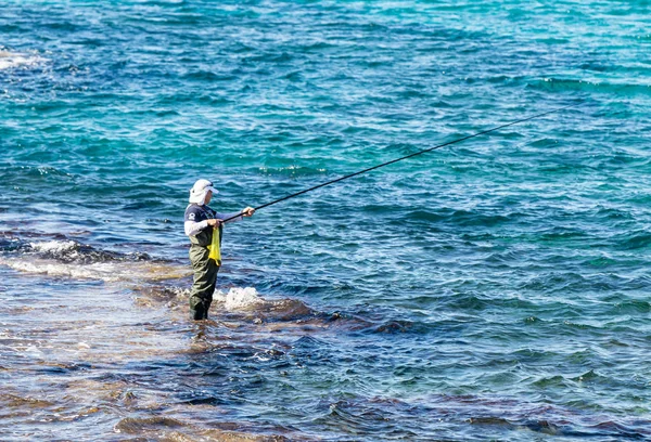 Un pêcheur en vêtements imperméables se tient genoux dans les eaux de la mer Méditerranée et attrape un poisson sur une pêche à Césarée, dans le nord d'Israël . — Photo