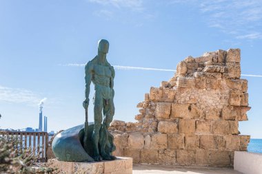 Küreğin bir parçasıyla çıplak bir adamı tasvir eden yeşil bir heykel Caesarea şehrinde, Akdeniz kıyılarında, kuzey İsrail 'de soyut bir şekilde yapılmış.