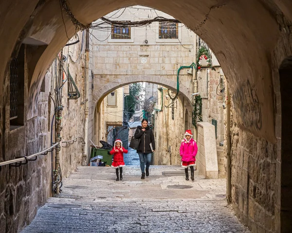 Mamá con hijas pequeñas vestidas con disfraces de Papá Noel camina por una calle desierta cerca de la Puerta de Jaffa en la Ciudad Vieja de Jerusalén, Israel — Foto de Stock