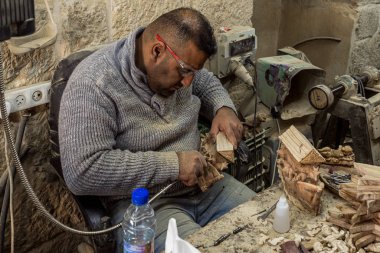 Bir marangoz atölyesinde oturuyor ve Filistin 'deki Beytüllahim' de ağaçtan dini hediyeler yapıyor.