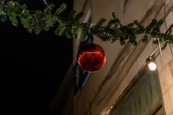Vista noturna de uma grande bola vermelha pendurada em um galho de árvore de Natal de plástico decorado para celebrações de Natal rua na parte antiga de Nazaré em Israel — Fotografia de Stock