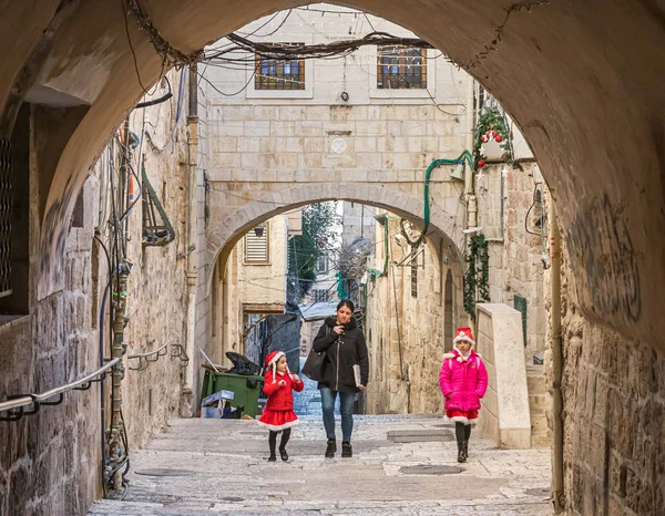 Mamá con hijas pequeñas vestidas con disfraces de Papá Noel camina por una calle desierta cerca de la Puerta de Jaffa en la Ciudad Vieja de Jerusalén, Israel — Foto de Stock