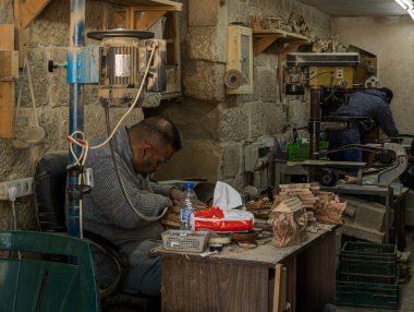Bir marangoz atölyesinde oturuyor ve Filistin 'deki Beytüllahim' de ağaçtan dini hediyeler yapıyor.