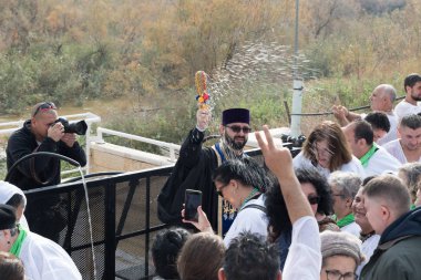 Rahip, İsrail 'deki Jericho yakınlarındaki Ürdün Nehri' ndeki İsa Mesih 'in Vaftiz Alanına inananların üzerine kutsal su serpiyor.