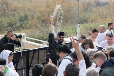 Rahip, İsrail 'deki Jericho yakınlarındaki Ürdün Nehri' ndeki İsa Mesih 'in Vaftiz Alanına inananların üzerine kutsal su serpiyor.