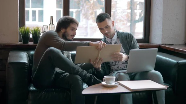 Two entrepreneurs working and taking notes together in table of a little office. Freelancer meeting, man with laptop drink coffee in coworking.