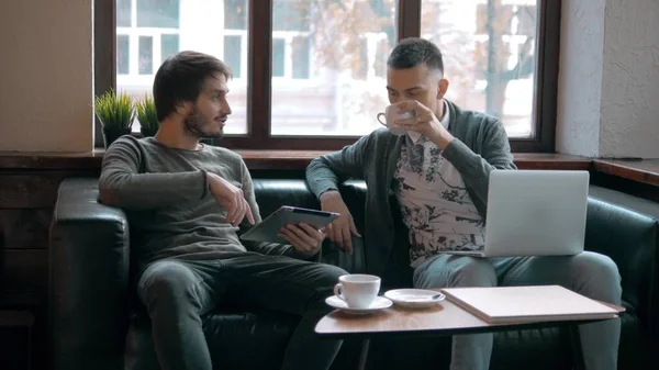 Two entrepreneurs working and taking notes together in table of a little office. Freelancer meeting, man with laptop drink coffee in coworking.