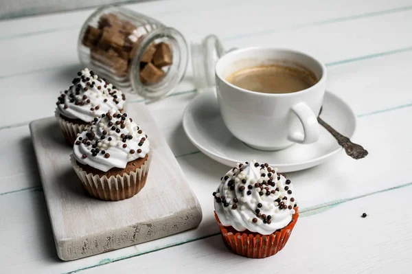Vanilla cupcakes with butter cream with chocolate topping and cup of coffee on a wooden chopping board on a light background