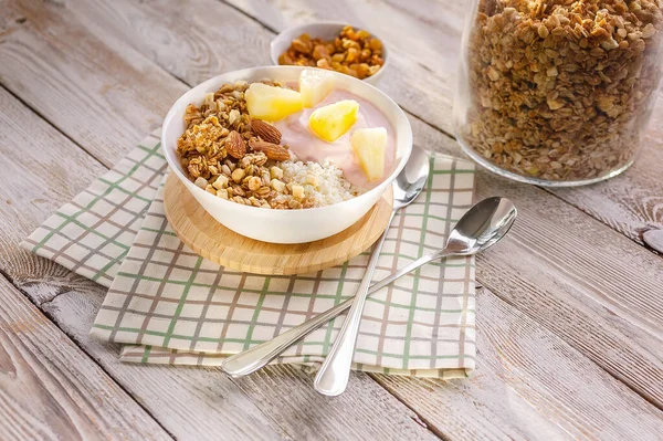 Baked granola with nuts, cottage cheese, strawberry yogurt and pineapple slices in a plate on a checkered napkin. The light of the morning sun. Healthy breakfast