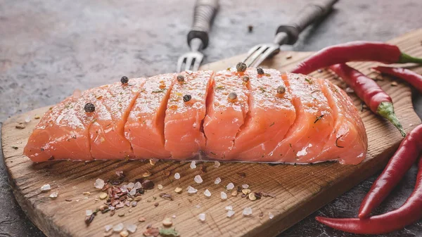 Food banner. Salted salmon piece on a wooden cutting board on a concrete brown background. Pepper and other spices.