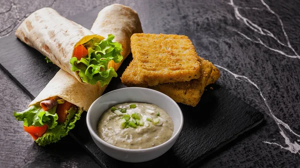 Food banner. Tortilla wrap with salmon and fresh salad, breaded fish fillet and sauce on a black cutting board