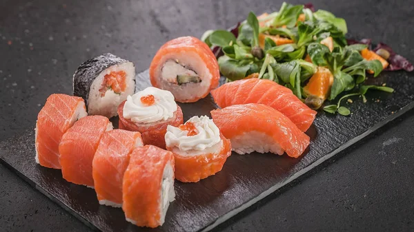 Horizontal food banner. Sushi and rolls with salmon and salad on a black flat tuff plate. Tasty oriental food