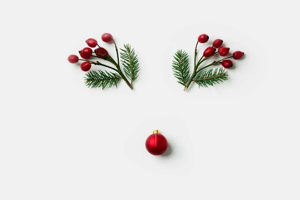 Cara de reno hecha de decoraciones navideñas, bayas de acebo y ramas de pino. Concepto mínimo. Puesta plana —  Fotos de Stock
