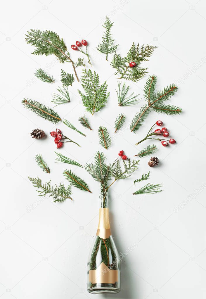 Champagne bottle with winter splash foliage on white background. Flat lay. Party concept.