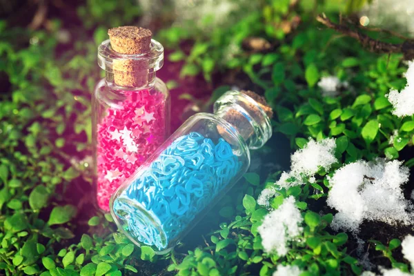 Dos botellas de vidrio con estrellas moradas y corazones azules en el bosque . —  Fotos de Stock