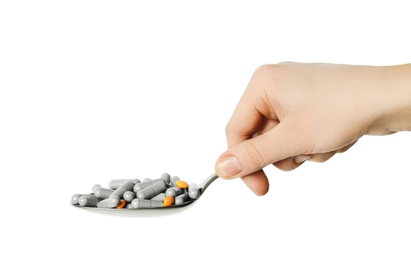 Ręka trzyma whith łyżkę, którą kapsułki białe i pomarańczowe tabletki — Zdjęcie stockowe