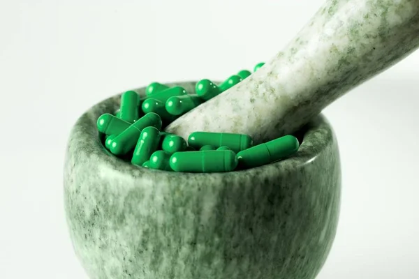 Green capsules and orange pills with mortar pestles on white background. — Stock Photo, Image