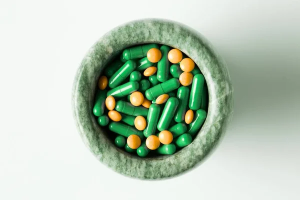 Capsules vertes et pilules orange avec pilons de mortier sur fond blanc . — Photo
