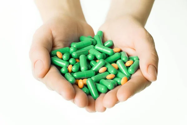 Ręce daje zielone kapsułki i tabletki pomarańczowy na białym tle. — Zdjęcie stockowe