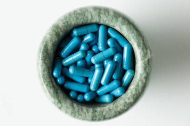 Mavi kapsül ve turuncu beyaz zemin üzerine harç dibekler haplarla.