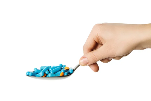 Рука держит ложку, голубые капсулы и оранжевые таблетки. — стоковое фото